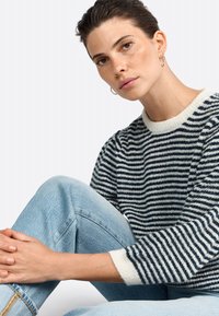 Striped sweater in navy and cream knit, with a ribbed crew neckline and long sleeves. Pair of light blue denim jeans visible.