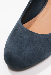 Pantofole blu in suede con punta arrotondata, texture liscia e tacco leggermente elevato. L'interno presenta una soletta color beige con dettagli di cucitura.