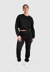 Zwarte cropped sweatshirt met textuuraccenten en bijpassende zwarte joggerbroeken met een elastische tailleband en manchetten, gecombineerd met witte schoenen.