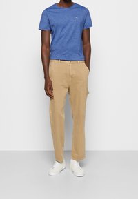 Camiseta azul de manga corta con un acabado texturizado, combinada con pantalones cargo de algodón beige que cuentan con bolsillos laterales y un ajuste relajado. Zapatillas blancas completan el look.