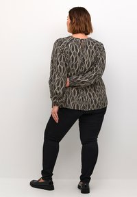 Långärmad topp i mörkbrun tyg med ett krämfärgat abstrakt mönster, med en nyckelhålsdetalj i ryggen. Kombineras med svarta slim-fit jeans och svarta loafers.
