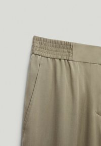 Pantalons en tissu léger beige avec une taille élastique froncée et des poches latérales. Texture lisse, forme fuselée, adaptés à un look décontracté.