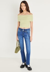 Svetlo zelena rebrasta kratka majica z odkritimi rameni, kombinirana z modrimi kavbojkami z ravnimi hlačnicami, dvojnim zapenjanjem na gumb in sprednjimi žepi. Torbica olivno zelene barve.