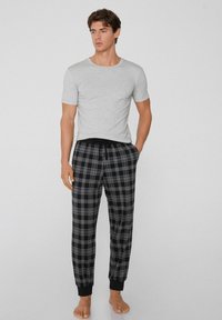 Grijze katoenen t-shirt gecombineerd met zwart-grijze geruite pyjamabroek. De broek heeft een elastische tailleband met trekkoord en taps toelopende boorden.