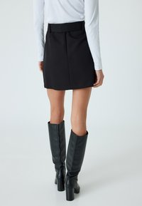 Zwarte mini-jurk met een aansluitende taille en lichte plooien. Gecombineerd met hoge zwarte leren laarzen met chunky hakken. Eenvoudig ontwerp.