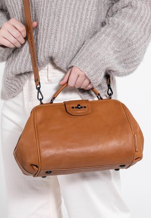 Tasche aus hellbraunem Leder mit strukturierter Form, Obergriff und abnehmbarem Schultergurt. Sie verfügt über einen schwarzen Verschluss, dezente Nähte und schütztende Füße.