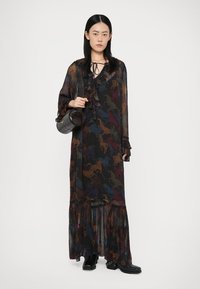 Lang, doorschijnende zwarte jurk met kleurrijke paardenpatronen, volants aan de halslijn, brede mouwen en een gelaagde zoom. Gecombineerd met een kleine zwarte tas en laarzen.