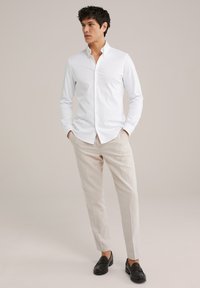 Hvid, langærmet skjorte med knapper, parret med lyse beige bukser og sorte loafers; glat stof og skræddersyet pasform. Minimalistisk design.