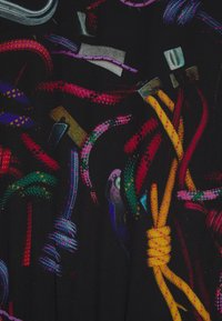 Corde intrecciate colorate in varie tonalità (viola, rosso, verde, giallo) su uno sfondo nero con clip e accessori metallici.