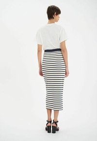 Jupe en tricot rayée avec des lignes horizontales bleu marine et blanches, ceinture côtelée, portée avec un t-shirt blanc uni et des sandales à talons carrés noires.