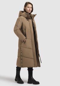 Garšs, mīkstu pildījumu apģērbs siltā beidža krāsā. Aprīkots ar kapuci, ar rāvējslēdzēju aizdari, sānu kabatām un spiedpogām gar apakšmalu. Gluda tekstūra.