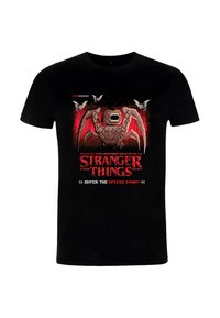 Camiseta de algodón negro con un diseño gráfico de un monstruo con acentos rojos, texto "Stranger Things" y murciélagos pixelados sobre un fondo desgastado.