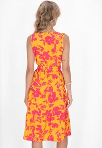 Rochie florală cu un fundal galben aprins și modele de flori roz, design fără mâneci, talie ajustată și fustă stratificată.