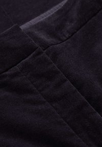 Temno žametno blago, ki prikazuje teksturo in sijaj z opaznimi detajli šivanja, z gladko, mehko površino in bogato barvo.