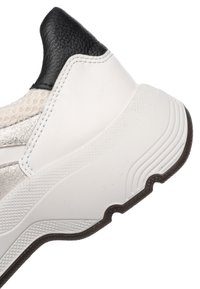 Gros plan sur le talon d'une basket blanche avec une semelle noire texturée, un col en cuir noir et un détail en mesh près de la cheville.