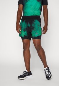 Svarta träningsshorts med grönt tie-dye-mönster, elastiskt midjeband och Adidas-logotyp. Bärs med svarta löparskor.