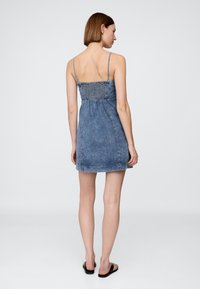 Riflové šaty s tenkými špagetovými ramínky, nařaseným živůtkem a střihanou rovnou sukní. Světle modrá barva s hladkou texturou.