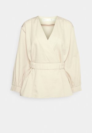 Top em bege com tecido texturizado, decote em V, cintura elástica e mangas longas com punhos franzidos. Detalhe de barra peplum.