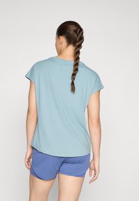 Top azul claro de manga corta con un ajuste holgado, combinado con pantalones cortos morados. El tejido parece suave y el diseño cuenta con un escote redondeado.