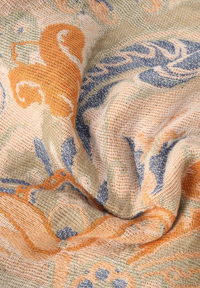 Gros plan sur un tissu beige tissé avec des motifs floraux texturés orange et bleu, montrant le tissage détaillé et les plis.
