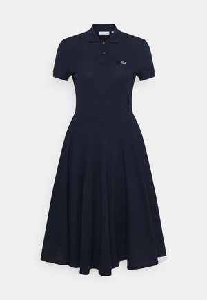 Robe polo bleu marine à manches courtes avec col boutonné, taille cintrée, jupe évasée et petit logo crocodile brodé sur la poitrine.