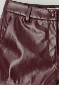 Jupe en cuir verni bordeaux au toucher lisse, dotée d'une fermeture à bouton et d'une poche sur le côté. Design ajusté avec une finition brillante.