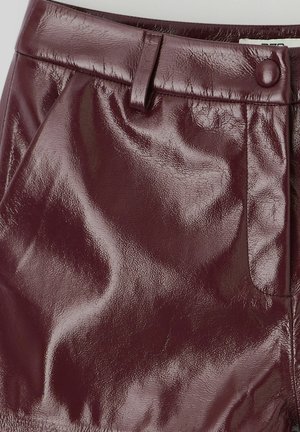 Jupe en cuir verni bordeaux au toucher lisse, dotée d'une fermeture à bouton et d'une poche sur le côté. Design ajusté avec une finition brillante.