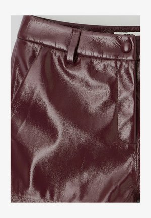 Jupe en cuir verni bordeaux au toucher lisse, dotée d'une fermeture à bouton et d'une poche sur le côté. Design ajusté avec une finition brillante.