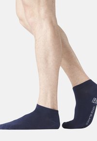 Chaussettes de cheville bleu marine en matériau tricoté doux et extensible. Présentent un poignet côtelé et une marque discrète sur le côté.