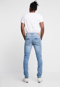 Světlé modré džíny s úzkým střihem, se zadními kapsami a koženou štíhlou značkou na pase, nošené s jednobarevným bílým tričkem.