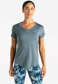 Camiseta deportiva de color gris claro con mangas cortas y cuello en V. Textura sutil; logo en el pecho. Combinada con leggings azules con estampado.