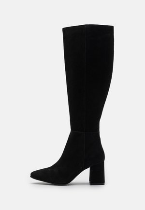 Botă neagră din suede, până la genunchi, cu vârf ascuțit, toc bloc și textură netedă. Trunchiul nu are hardware vizibil sau embellishments.