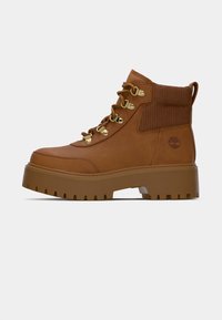 Bottines marron en cuir, dotées d'une semelle en caoutchouc texturée, d'un matériel de laçage en métal et d'un col côtelé. Logo signature sur le côté.