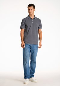 Szary polo z trzema guzikami, kontrastowym wykończeniem kołnierzyka oraz subtelnym logo. Połączony z niebieskimi dżinsami i białymi sneakersami.