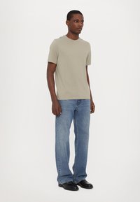 Lys grå bomull T-skjorte med korte ermer, kombinert med blå denimjeans og svarte sko. Enkelt design uten synlige logoer.