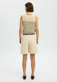 Light beige sleeveless top with black stripes, paired with light beige shorts. Soft material, relaxed fit, and black belt at the waist.