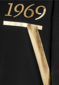 Tela negra con estampado metálico dorado que presenta "1969" en la parte superior y una "T" en negrita que se extiende en diagonal. Textura suave con un acabado brillante.
