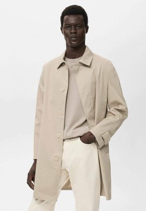 Giacca leggera beige con colletto e sei bottoni, abbinata a una camicia crema e pantaloni chiari, indossata da un modello.