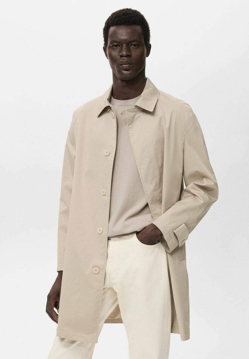 Chaqueta ligera beige con cuello y seis botones, combinada con una camisa crema y pantalones de color claro, exhibida en un modelo.