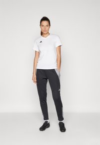 White athletic t-shirt with black logo, paired with dark grey joggers featuring light grey accents and black sneakers with laces.