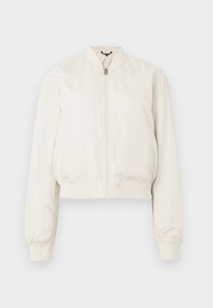 Īss bumbvedēja stila jaciņa neitrālā krēmkrāsā, ar rāvējslēdzēju priekšpusē, stāvkrānu un ribotām aprocēm, ar gludu un matētu virsmu.