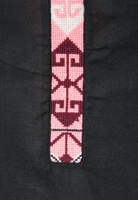 Schwarzer Stoff mit einem zentralen gewebten Design in Pink und Burgunderrot, das geometrische Muster und kontrastierende Texturen zeigt.