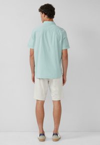 Helles blaues kurzärmliges Hemd aus Baumwolle, kombiniert mit beigen Shorts. Das Hemd hat eine weiche Textur und einen klassischen Kragen.