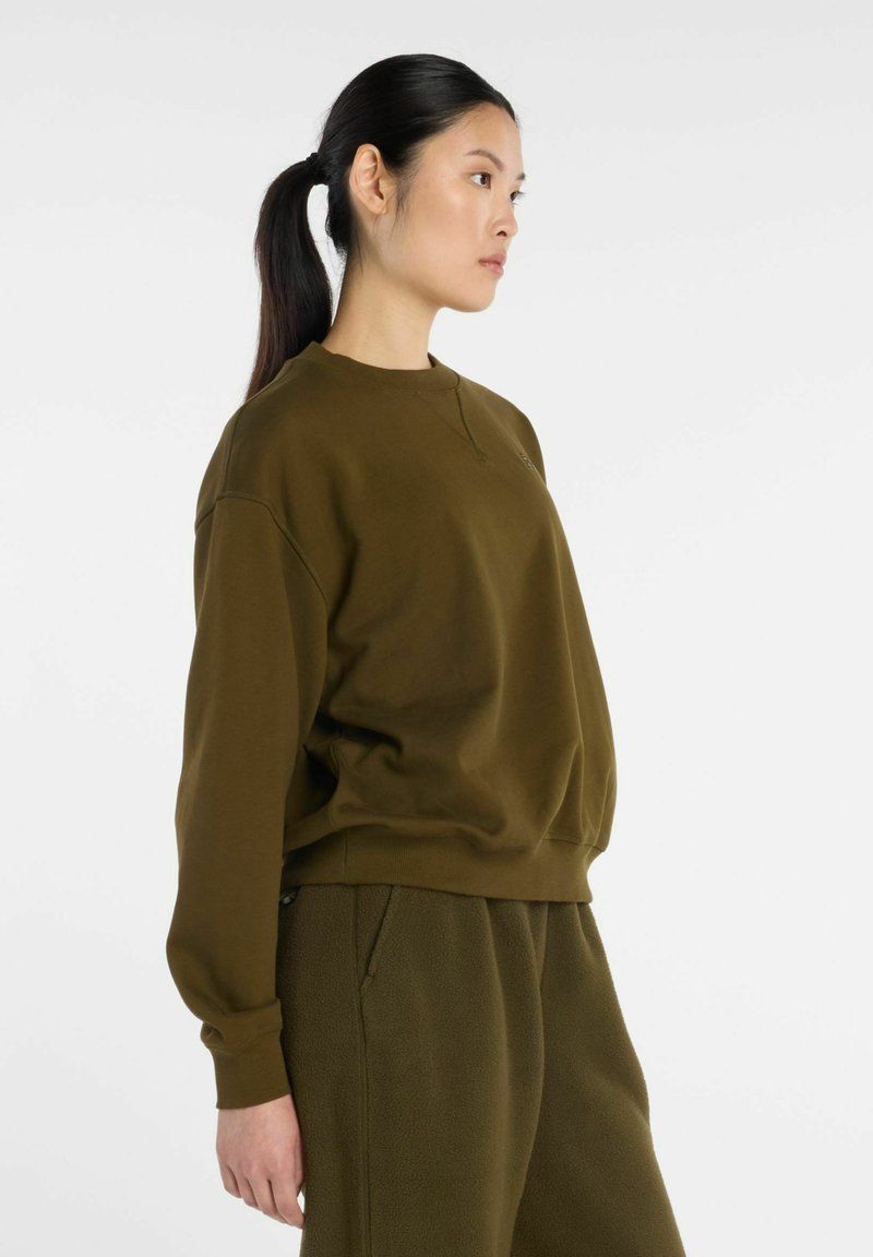 Sweat-shirt vert olive avec un col rond, une coupe décontractée et des poignets côtelés. Présente une texture de tissu lisse et un design minimaliste.
