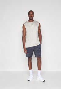 Camiseta atlética sin mangas de color beige claro con patrón geométrico; pantalones cortos azul marino con un diseño sutil; zapatillas deportivas y calcetines blancos.