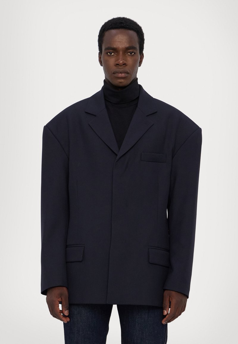 Übergroßer navy Blazer mit strukturierten Schultern, einer Brusttasche und zwei Fronttaschen. Texturiertes Material und breite Revers.