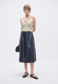 Top fără bretele crem cu buline negre, asortat cu o fustă midi albastru închis lucioasă. Modelul ține o poșetă mică neagră și poartă balerini negri.