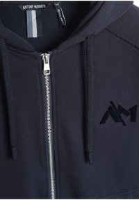Felpa con zip navy realizzata in tessuto morbido, con zip frontale, cappuccio con coulisse e logo ricamato sul petto. Design a vestibilità regolare.