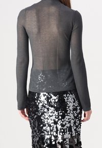 Haut gris à manches longues côtelé avec un dos transparent. Associé à une jupe noire ornée de sequins qui reflètent la lumière.