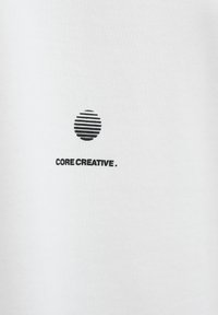 T-shirt en coton blanc avec un graphique noir de lignes concentriques formant un cercle au-dessus du texte "CORE CREATIVE." en gras.